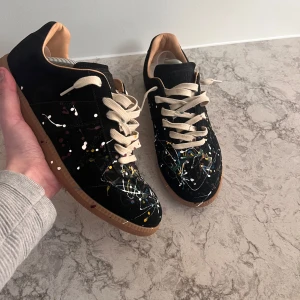 Svarta sneakers med färgstänk och beige sula - Unika svarta sneakers med färgstänk i vitt, blått, gult och rött. Skorna har beige snörning och sula, samt rund tå. Perfekta för dig som vill sticka ut med din stil.