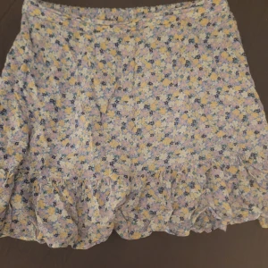Blommig kjol med volang från Pieces - Supersöt blommig kjol från Pieces i ljusblått, gult och vitt. Kjolen har volang längst ner och en kort passform som känns perfekt för varmare dagar. Blommigt mönster ger en fräsch och somrig vibe.