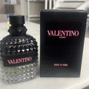 Valentino Uomo Born In Roma 100ml - Säljer en lyxig parfym från Valentino, Uomo Born In Roma. Flaskan är 100 ml och har en cool, nitar-inspirerad design i svart och transparent glas. Märket syns tydligt med rosa text på svart etikett. Kommer med originalkartong.