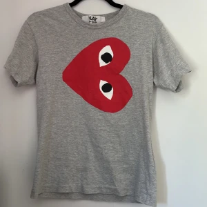 Grå Comme des Garçons Play t-shirt - Grå t-shirt från Comme des Garçons Play med  rött hjärta med ögon tryckt på bröstet. säljer denna tröja eftersom den inte passar mig längre. Storleken är small. Hör av er vid funderingar!🙃