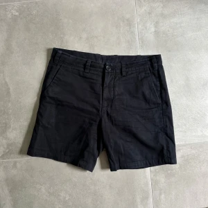 Mörkblå Arket shorts stl 48 - Klassiska mörkblå shorts i slim fit med snygg midja och bälteshällor. Modellen har två sidofickor fram och två bakfickor med knapp. Perfekta för en clean och stilren look under varmare dagar. Artnr: A338