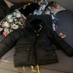 Svart dunjacka från Fjällräven XXS - Säljer en svart dunjacka från Fjällräven i storlek XXS. För den är förstor för mig. Den är man men passar även för kvinnor. Jackan har huva, dragkedja, stora fickor med lock och coola gula snören nertill. Perfekt för kalla dagar när du vill hålla stilen och värmen. Klassisk design med diskret logga på bröstet. Är även öppen för byte. Den är i bra skick