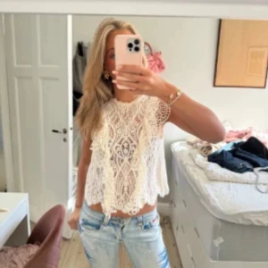 Vit spetsblus med volang från Zara - Superfin vit blus i spets från Zara med snygga volangdetaljer på axlarna och ett vackert mönster. Ärmlös modell med rund halsringning och knäppning bak i nacken. 