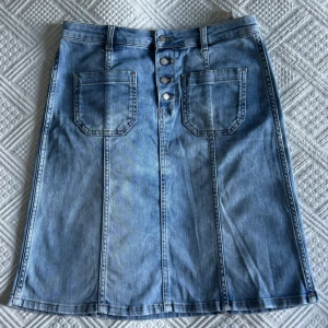  Jeanskjol  - Ljusblå jeanskjol från Boomerang med raka sömmar, stora framfickor och fyra snygga knappar framtill. Klassisk denimlook med bälteshällor och en liten läderpatch bak i midjan. Perfekt till sneakers eller boots.