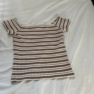 Randig stickad topp från Nelly - Använd 1 gång Superfin stickad topp från Nelly i storlek S. Toppen har bruna och vita ränder, korta ärmar. Materialet är mjukt och stickat, perfekt för en chill och trendig look. Passar perfekt till jeans eller kjol för en avslappnad stil. Det är en of shoulder tröja men man kan ha den som en vanlig med💕