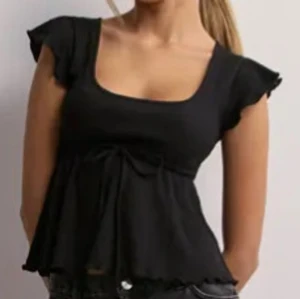 Svart blus med volangärm och knyt - Supersöt svart blus från Nelly med volangärmar och knyt under bysten. Den har en vid, flowy passform och rundad urringning. Perfekt till jeans eller kjol för en chill och snygg look.