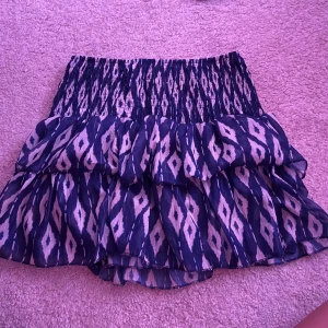 Blå mönstrad volangkjol - Supersöt kort volangkjol i blått och vitt med elastisk smock i midjan. Kjolen har ett grafiskt mönster och är luftig med flera lager volanger. Perfekt för dig som gillar en lekfull och trendig stil. Köpt i spanien o finns ingen lapp på! 