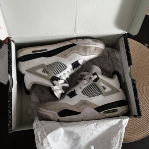 Air Jordan 4 vita och grå sneakers - Snygga Nike Air Jordan 4 sneakers i vitt och grått med svarta detaljer. Klassisk siluett med meshpaneler och coola plastdetaljer på sidorna. Skorna har snörning och en bekväm platt sula, perfekta för dig som gillar streetstyle.