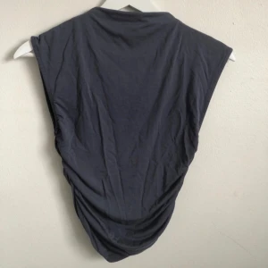 Mörkgrå topp  - Säljer en stilren mörkgrå ärmlös topp från Gina Tricot. Toppen har en enkel och clean design med lätt drapering i sidorna och breda axlar. Perfekt att matcha med jeans eller kjol för en cool look.