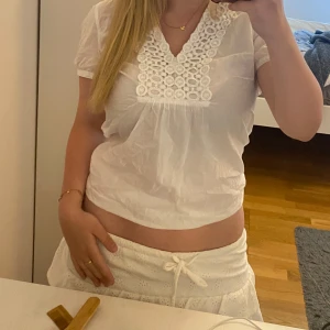 Vit blus med spetsdetaljer - Säljer en söt vit blus med korta ärmar och v-ringning. Framsidan har fina spetsdetaljer och broderade mönster. 