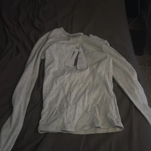 Ljusgrå långärmad tröja från Gina tricot  - En basic ljusgrå långärmad tröja från Gina tricot mjuk bomull. Enkel och clean design med rund halsringning, perfekt att styla med jeans eller under en jacka. Snygg passform och skön känsla mot huden.