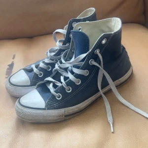 Blå converse - Klassiska höga sneakers i mörkblå canvas med vita gummisulor och tå, samt vita snören. Skorna har rund tå och tydliga kontrastsömmar. Perfekta för en avslappnad streetstil. BLIR TVÄTTADE INNAN DE SKICKAS!!