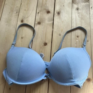 Ljusblå ribbad bh från Censored - Snygg ljusblå bh från Censored med ribbad struktur och justerbara axelband. Kuporna är vadderade och ger bra stöd. Perfekt för dig som vill ha en enkel men stilren bh med lite extra detalj i tyget.
