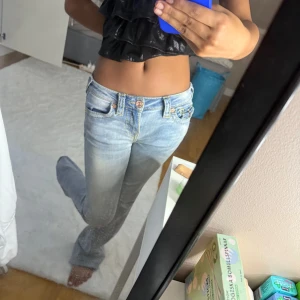 True Religion ljusblå bootcut jeans - Säljer ett par ikoniska ljusblå jeans från True Religion med snygga kontrastsömmar och klassiska fickdetaljer. Modellen har låg midja, bootcut-ben och coola kopparfärgade knappar. Perfekta för dig som gillar streetstyle och vill sticka ut. Väldigt bra hand om tagna! 