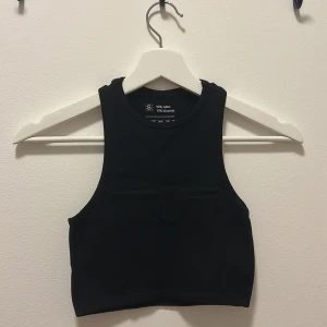 Svart croppad linnetopp - En svart, croppad linnetopp med ärmlös design och rund halsringning. Tillverkad i en mjuk och stretchig bomullsblandning som sitter skönt mot kroppen. Perfekt att matcha med höga jeans eller kjol för en clean look.