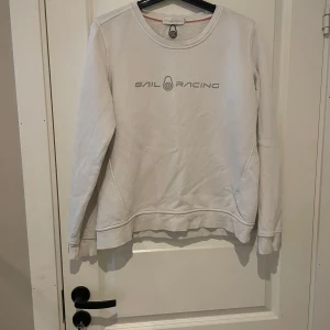 Vit Sail Racing sweatshirt i bomull - Vit sweatshirt från Sail Racing med rund hals och tryckt logga framtill. Tröjan är i mjuk bomull och har långa ärmar samt diskreta sömdetaljer. Perfekt för en clean och sportig stil. Passar perfekt för dig som vill ha en tröja inför hösten. Obs: har en svart prick vid vänster axel.  ( köp på Vinted brage2011)