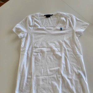 Vit v-ringad t-shirt Ralph Lauren - Vit v-ringad t-shirt från Ralph Lauren Sport i 100% pima bomull. Klassisk passform med korta ärmar och liten blå broderad logga på bröstet. Perfekt basic-plagg med mjukt material och stilren look.