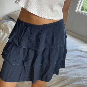 Mörkblå volangkjol med resår - Supersöt mörkblå kortkjol med flera volanger och resår i midjan. Kjolen har en luftig känsla och är perfekt för varma dagar. Passar till crop tops och sneakers för en chill look. Fint skick💗köpt i Italien🌸