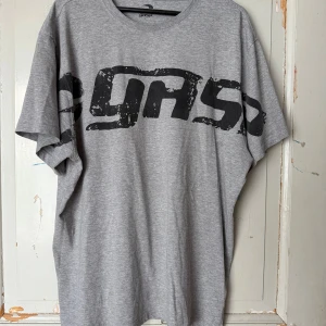 Grå t-shirt från Gasp med tryck - Säljer en grå t-shirt från Gasp med stort svart logotryck över bröstet. T-shirten har en loose passform och är tillverkad i mjuk bomull. Perfekt för dig som gillar sportiga och avslappnade plagg.