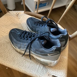 Nike Air Max 95 svarta sneakers - Svarta Nike Air Max 95 sneakers med vågformade paneler, mesh- och syntetmaterial samt synlig Air-sula. Klassisk snörning och diskret Swoosh på sidan. Perfekta för dig som gillar streetstyle och sportig vibe.