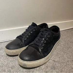 Marinblå Lanvin skor  - Stilrena marinblåa sneakers med ovandel i mocka och tåparti i skinn. Skorna har vita sulor och svarta snören, samt metallfärgade öljetter. Perfekta för en clean och avslappnad look. Pris går att diskuteras