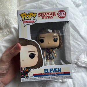 Stranger Things: Eleven (Pop! Television #802) - Samlarfigur av Eleven från Stranger Things, perfekt för fans av serien! Den ikoniska karaktären i färgglad klänning, levereras i originalförpackning. En cool detalj till din hylla eller skrivbord – ett måste för dig som älskar popkultur och Netflix-serier. Pris kan diskuteras!