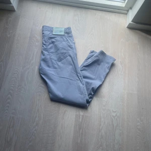 Ljusblå byxor från Jacob Cohën - Snygga ljusblå byxor från Jacob Cohën med raka ben och klassisk femficksdesign. Byxorna har silverfärgade knappar och är tillverkade i ett mjukt bomullstyg som känns riktigt skönt. Perfekta för dig som gillar stilrena och bekväma plagg.