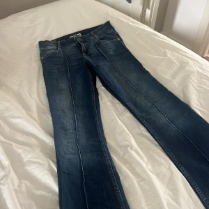 Blå bootcut jeans med låg midja - Snygga blå jeans med bootcut-modell och markerad låg midja. Jeansen har klassiska fem fickor, dubbla silverknappar och tydliga sömmar längs benen. Materialet är robust denim med lätt slitning för en cool look. Aldrig använda. Pris kan diskuteras 