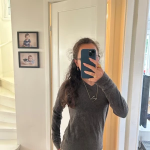 Mörkgrå stickad v-ringad tröja - Mysig mörkgrå stickad tröja med v-ringning. Tröjan har lång ärm och en klassisk, enkel design som passar till det mesta. Perfekt för lager-på-lager och chill dagar.