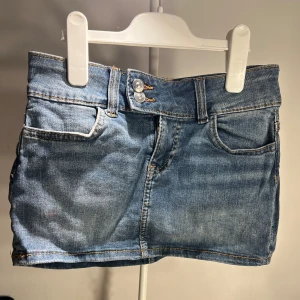 Blå jeanskjol från Divided H&M - Snygg blå jeanskjol från Divided by H&M med klassisk femficksdesign, dubbla knappar och dragkedja framtill. Kort modell med bälteshällor och coola kontrastsömmar. Perfekt till sneakers eller boots för en chill look.