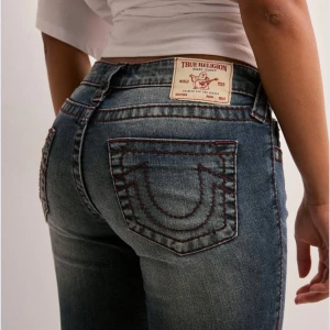 True Religion lågmidjade jeans  - Snygga blå bootcut jeans från True Religion med ikoniska bakfickor, Låg midja och klassisk femficksmodell. Strl w25. Bra skick men har små bristningar längst ner.