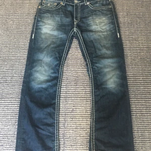 True Religion straight jeans blå, stl 38 - TVÄR coola blå jeans från True Religion med tydliga kontrastsömmar och ikoniska bakfickor. klassisk femficksdesign och är tillverkade i kraftigt denimtyg. Perfekta för dig som gillar streetwear vibes.