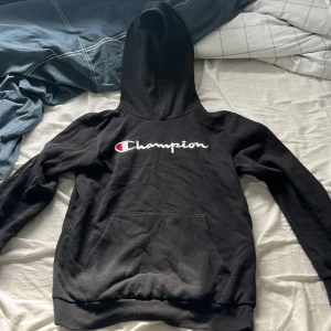 Svart Champion hoodie med broderad logga - Svart hoodie från Champion i storlek X-Large. Klassisk modell med stor broderad Champion-logga på bröstet, huva och känguruficka framtill. Mjuk och skön, perfekt för chill dagar. Passar dig som gillar streetwear och enkel stil.