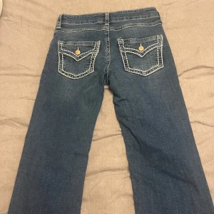 Blå jeans från Gina Tricot - Säljer ett par blå jeans från Gina Tricot med snygga kontrastsömmar och fickor med lock och knapp bak. Jeansen har klassisk femficksdesign och raka ben. Perfekta för dig som gillar en enkel men ändå unik look.💕💕Storlek 170 dvs S