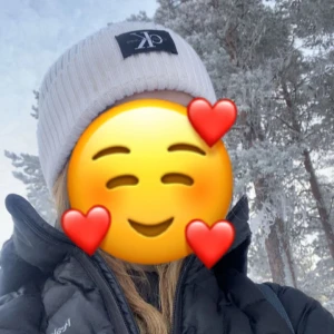 Vit ribbad mössa från Calvin Klein - Vit ribbstickad mössa från Calvin Klein med svart logotyp-patch framtill. Klassisk och enkel design som passar perfekt till kalla dagar. Snygg och stilren accessoar för vintern.