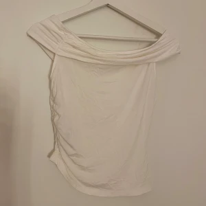 Vit offshoulder topp - Snygg vit offshoulder topp med bred krage som vilar över axlarna. Toppens passform är figurnära. Materialet känns mjukt och stretchigt, vilket gör den bekväm att bära.