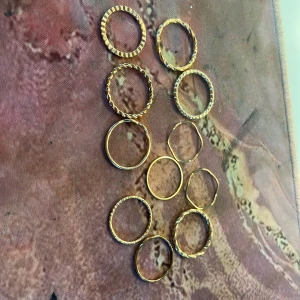 Set med tunna guldiga ringar - Säljer ett set med tio tunna ringar i guldig färg. Ringarna har olika mönster, bland annat tvinnade och randiga detaljer. Perfekta att mixa och matcha på olika fingrar för en trendig look.