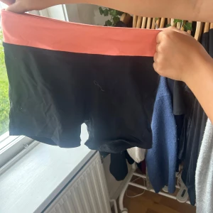 Svarta shorts med rosa midja - Snygga svarta shorts med bred rosa midja. Modellen är tight och passar perfekt för träning eller sport. Materialet känns stretchigt och bekvämt, vilket gör dem smidiga att röra sig i. Midjan är hög och ger en schysst passform.