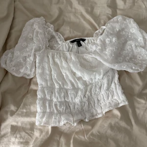 Vit blus med puffärmar och broderi - Superfin vit blus från vero Moda med puffiga korta ärmar och broderade blommor över hela tyget. Toppen är croppad. Toppen är använd en gång. Passar även för dig med strl xs 