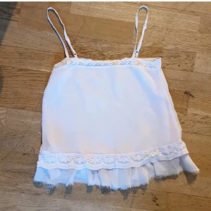 Ljusrosa linnetopp med spets och volang - Supersöt ljusrosa linnetopp med tunna justerbara axelband, spetsdetaljer upptill och nertill samt volangkant längst ner. Toppens material är lätt och luftigt, perfekt för varma dagar. Ger en romantisk och feminin vibe.