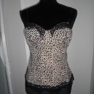Leopardmönstrad korsett topp med spets - Snygg leopardmönstrad korsett med svarta spetsdetaljer upptill och nedtill. Axelbanden är justerbara och toppen har en figurnära passform. Aldrig använd!