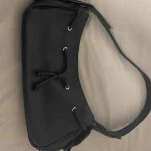 En för 20 båda för 30 - Säljer två svarta axelväskor. Ena väskan har slätt material med snörningsdetaljer och silvriga öljetter. Den andra har croco-mönstrad yta och en grov silvrig kedja som axelrem. Båda har en modern, böjd form och passar perfekt till en trendig look.