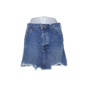 Blå jeanskjol från Bershka - Snygg blå jeanskjol från Bershka Vintage Collection med rå kant nertill och klassiska fickor både fram och bak. Kjolen är i kort modell och har en avslappnad vibe, perfekt till sneakers eller boots. Gjord i 100% bomull. 