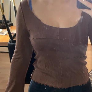 Brun långärmad topp från Monki - Säljer en brun långärmad topp från Monki med utsvängda ärmar och vågiga sömmar som ger en cool, edgy vibe. Toppen har ribbad struktur, croppad passform och fyrkantig urringning. Perfekt för dig som gillar trendiga detaljer och vill sticka ut.