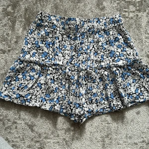 Blommiga shorts från Zara i blått och vitt - Snygg kjol från Zara med blommigt mönster i blått, vitt och svart. Den har inbyggda shorts under volangen vilket gör det bekvämt att ha på sig! Skriv vid frågor💗🌟