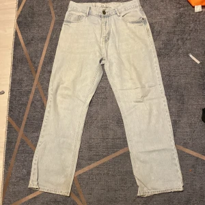 Ljusblå raka jeans från Zara - Säljer ett par ljusblå jeans från Zara med klassisk femficksdesign och raka ben. Jeansen är tillverkade i bomullsdenim och har en snygg vintagekänsla. Perfekta för en avslappnad och trendig look.