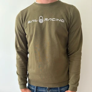 Olivgrön långärmad tröja Sail Racing - Olivgrön långärmad tröja från Sail Racing med vit logga tryckt över bröstet. Skön och snygg! 