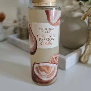Victoria's Secret Coconut Passion Brûlée - Fräsch body mist från Victoria's Secret i doften Coconut Passion Brûlée. Doftnoter av kokosflingor och brun socker ger en söt, tropisk vibe. Flaskan är genomskinlig med beige och bruna detaljer, rymmer 250 ml och har en stilren, rund form. Helt ny och oanvänd. Inga prisförslag accepteras.