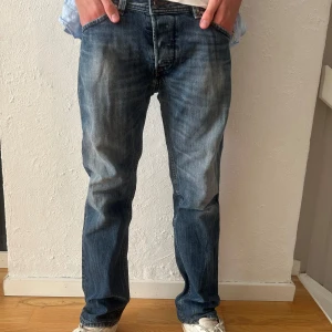 Diesel Darron blå jeans regular tapered - Säljer ett par blå Diesel Darron jeans i regular tapered fit. Jeansen har klassisk femficksdesign, snygg tvätt med slitningar och raka ben. Materialet är robust denim i bomull och passformen är avslappnad.