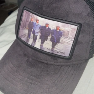 Svart Maggiore keps med mesh och print - Svart keps från Maggiore, knapparna där bak på kepsen är lite trasiga så sänker ju priset med den funkar ändå.